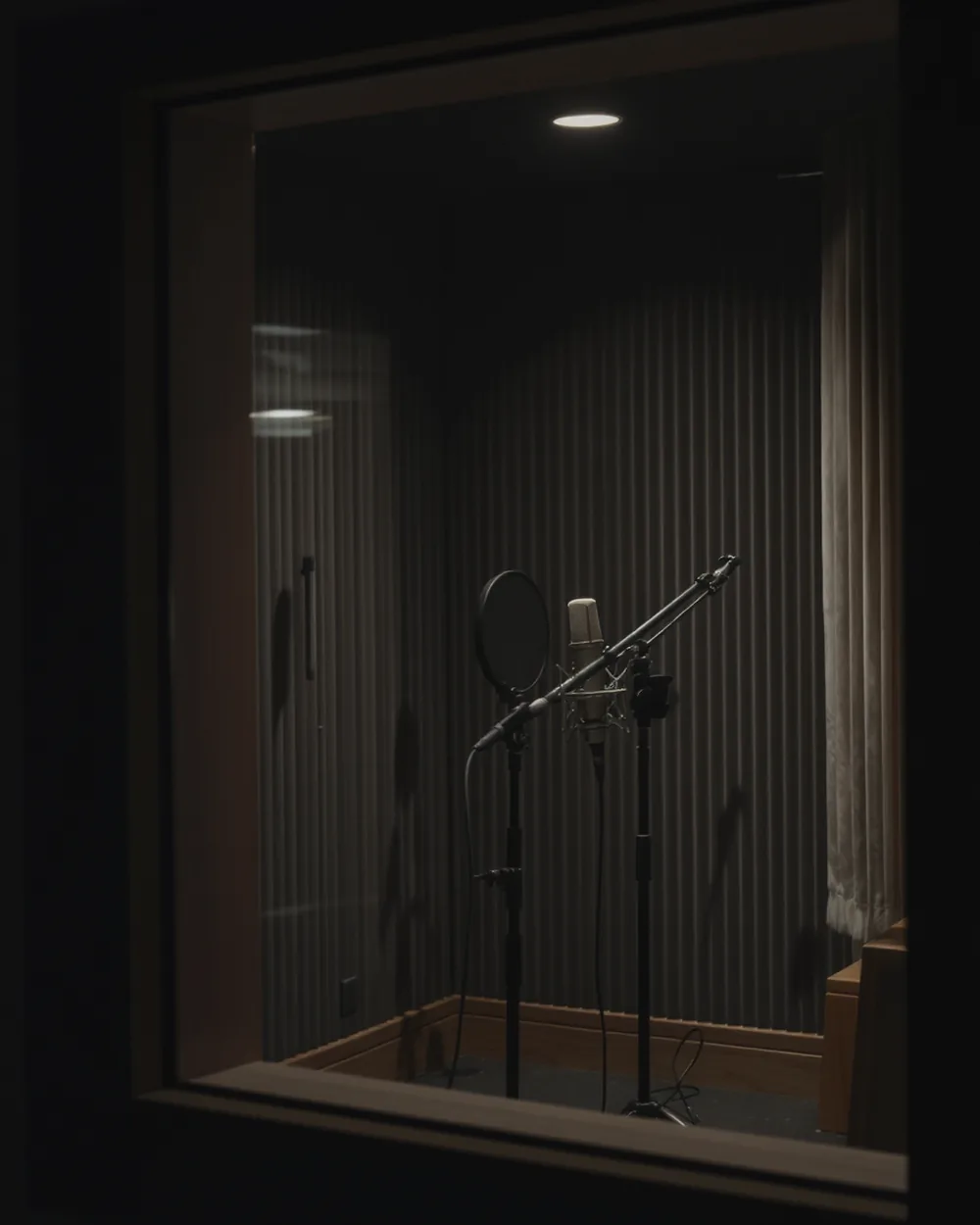 Vocal booth seen through the control room glass, condenser microphone on a boom.